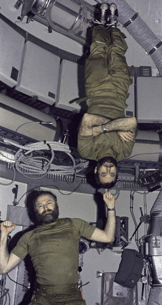 Gerald Carr demonstrates weight training in zero gravity by balnacing felkow astronaut William Pogue upside down on his finger.