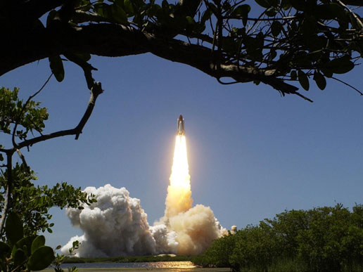 Space Shuttle Discovery's liftoff is reflected in the nearby water, as it ascends on the first ever launch on Independence Day.